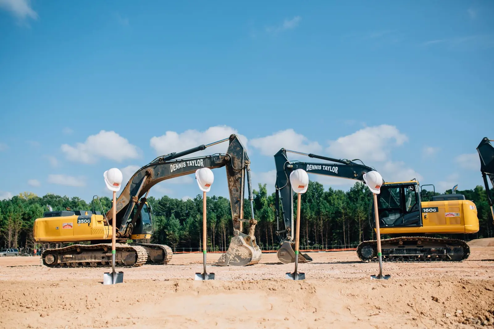 Two Dennis Taylor excavators at a groundbreaking with hard hats and shovels